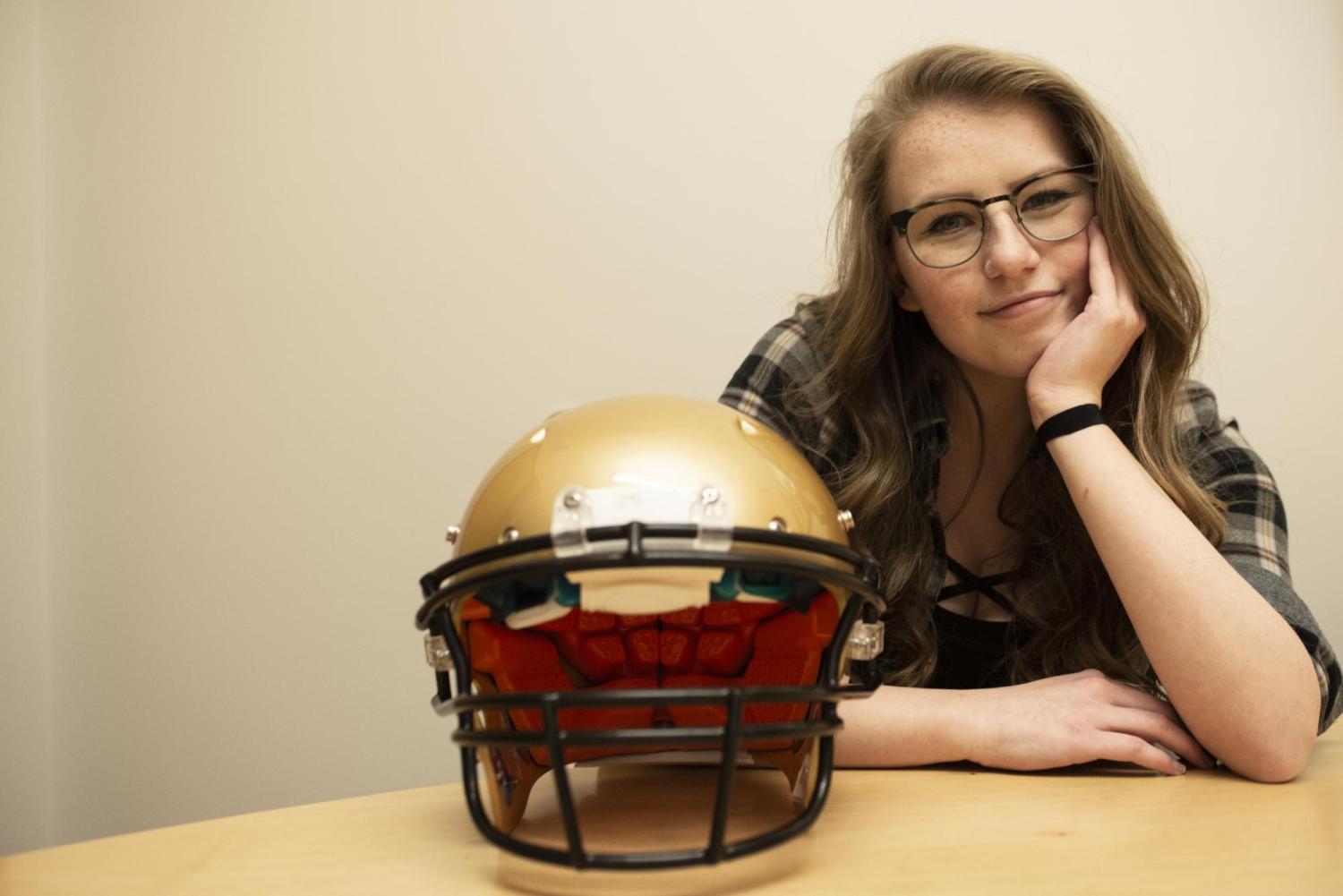 Kailey Epp sits next to a football helmet.