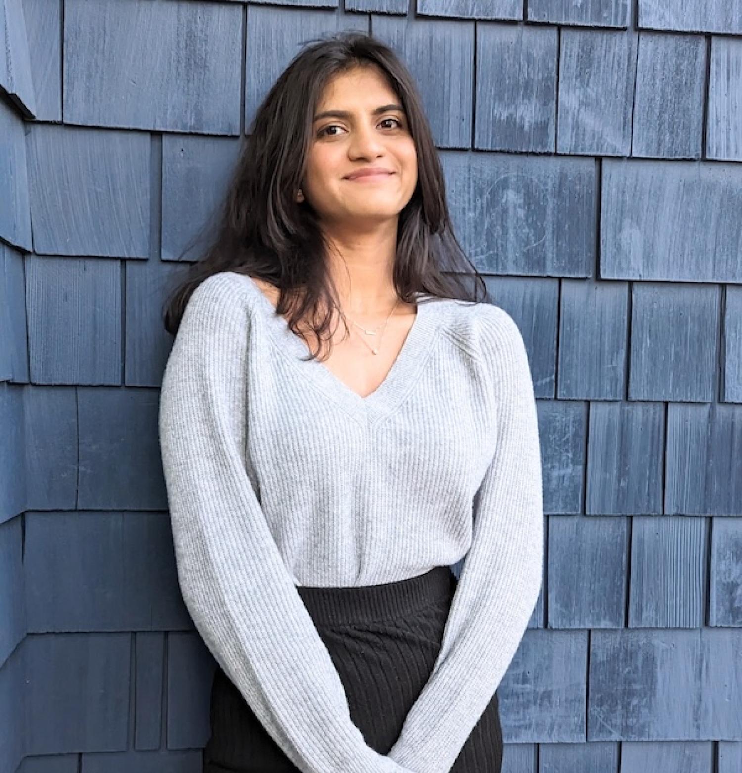 Aarya standing against a shingled wall smiling