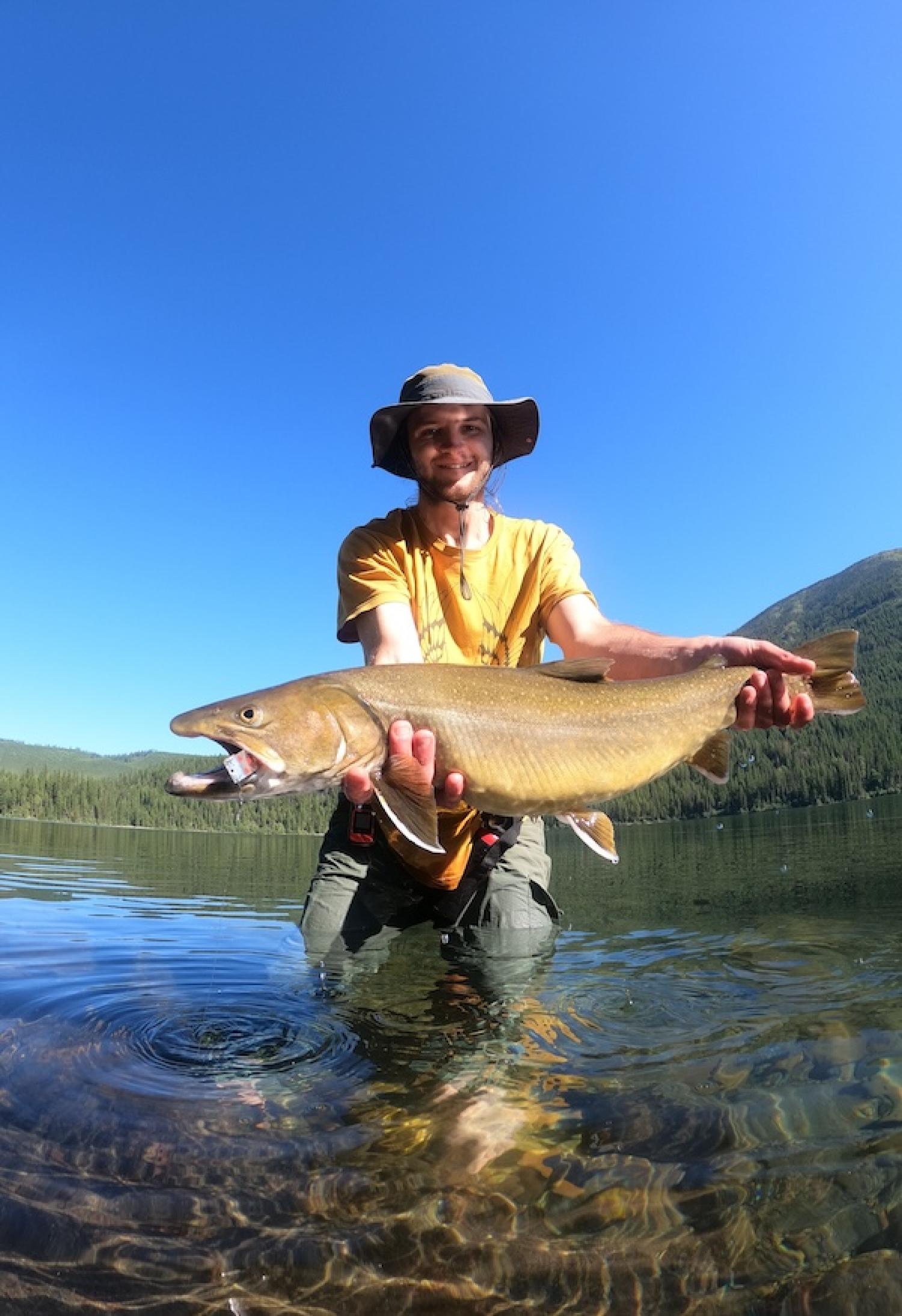Reagan McKee holding a large fish in a shallow river on a sunny day