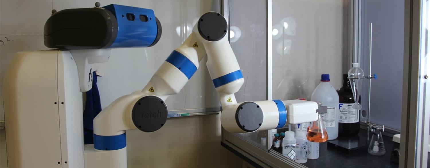 Robochemistry robot arm holding a flask of brown liquid in a wet lab
