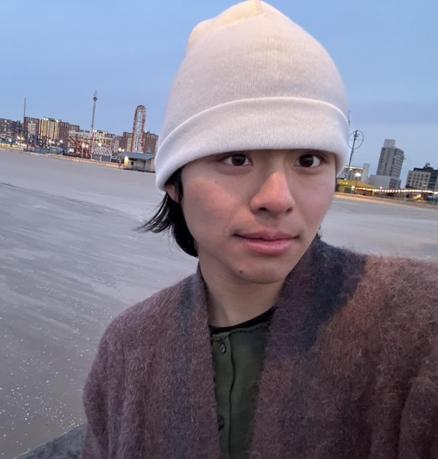 Yekun standing on a beach in cold weather with a city skyline behind
