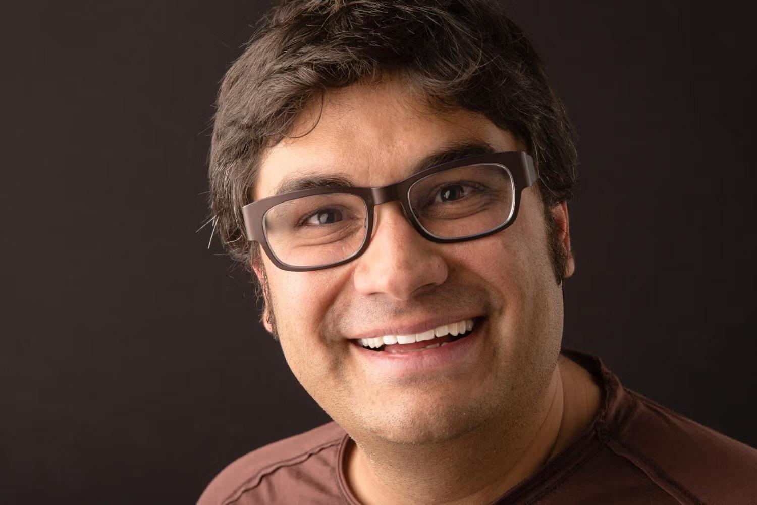 Profile of a white man smiling. He is wearing glasses and a burgundy shirt.