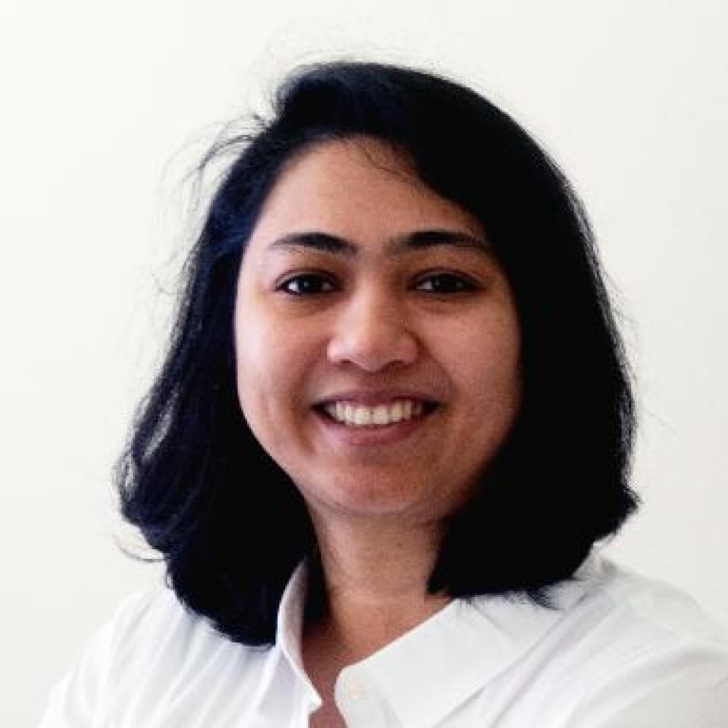 A profile of a brown woman with a black bob, smiling. She is wearing a white shirt.