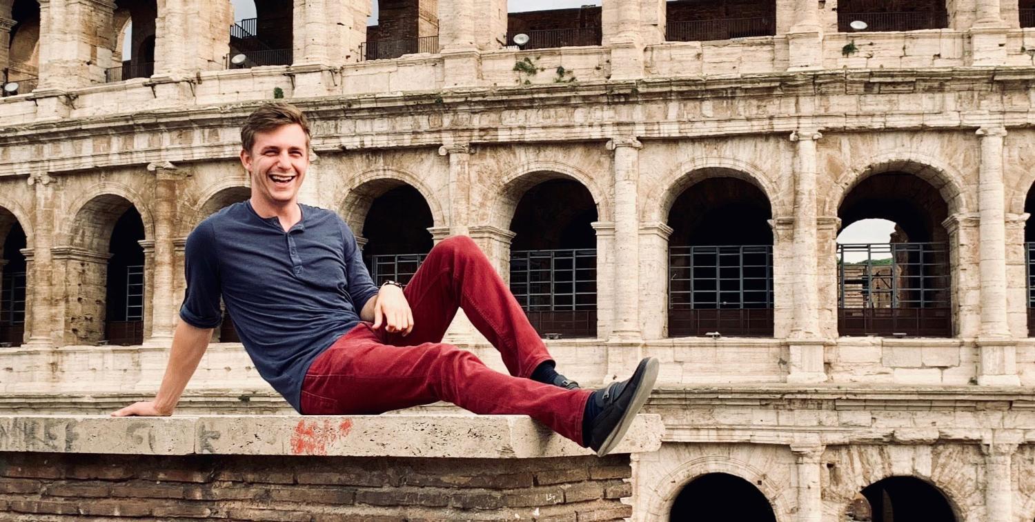 White man laying on a ledge, surrounded by old architecture.