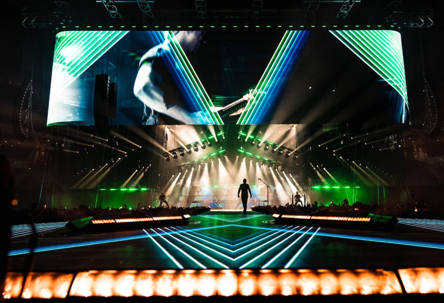 Image of a dark stage lit by bright technicolor blue-green lights. A person's silhouette is visible in the center.