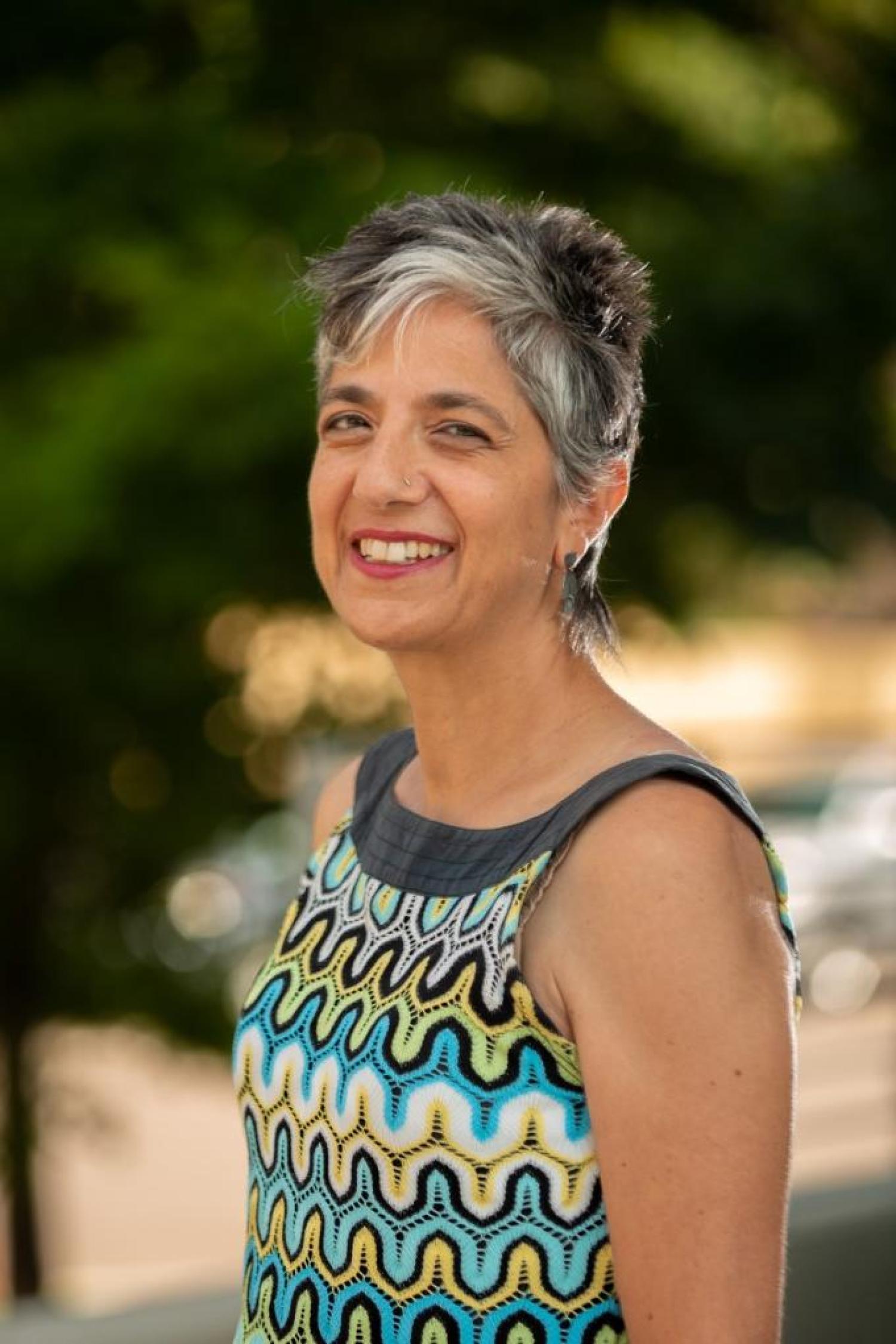 Profile image of an older woman with short gray hair, smiling and wearing a colorful tanktop
