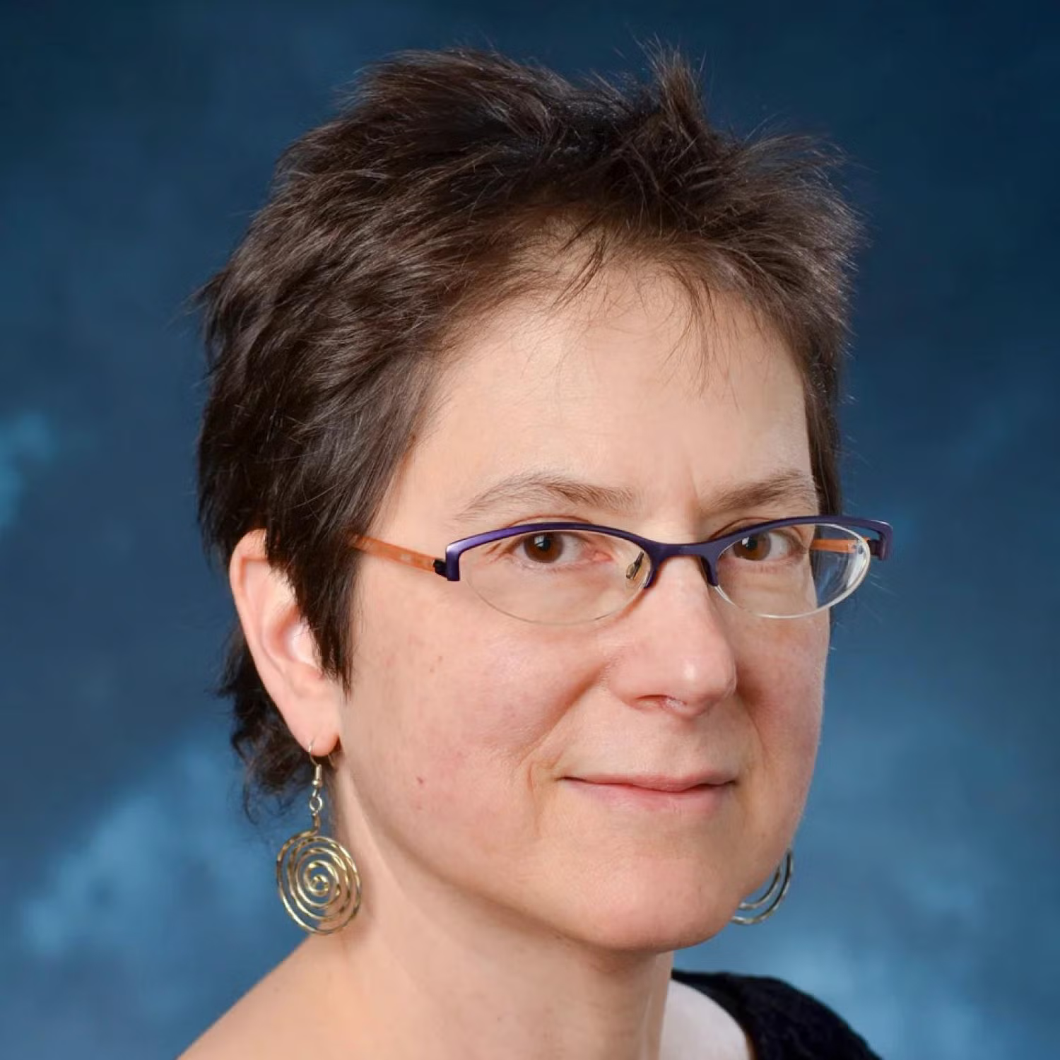 Profile of an older white woman with short brown hair, wearing glasses and smiling.