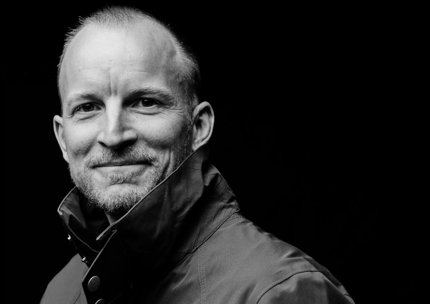 Black and white profile of a middle-aged man with thin short hair, smiling. He is wearing a high collar jacket.