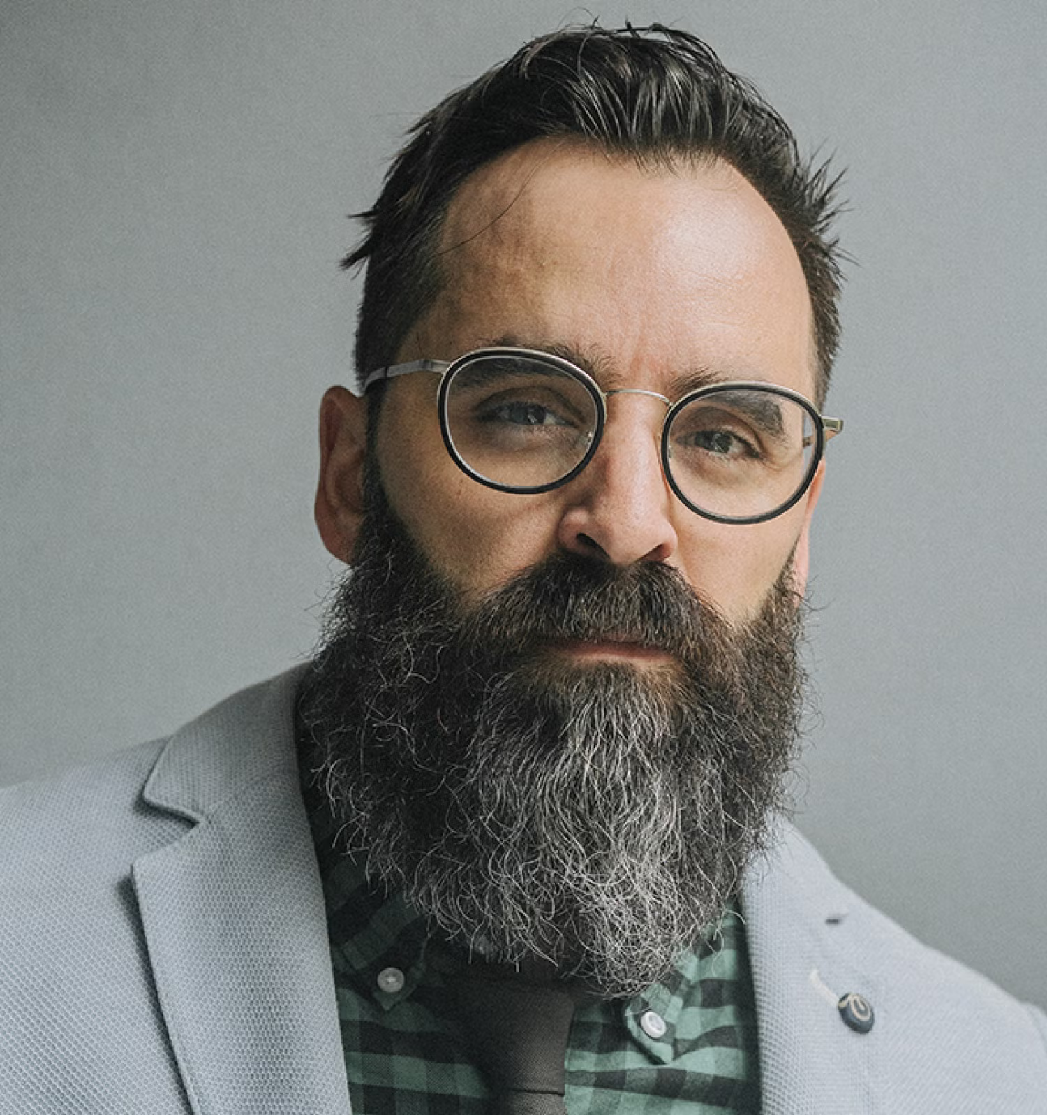 Man with short gray hair and a long gray beard. He is wearing glasses and a gray suit jacket.