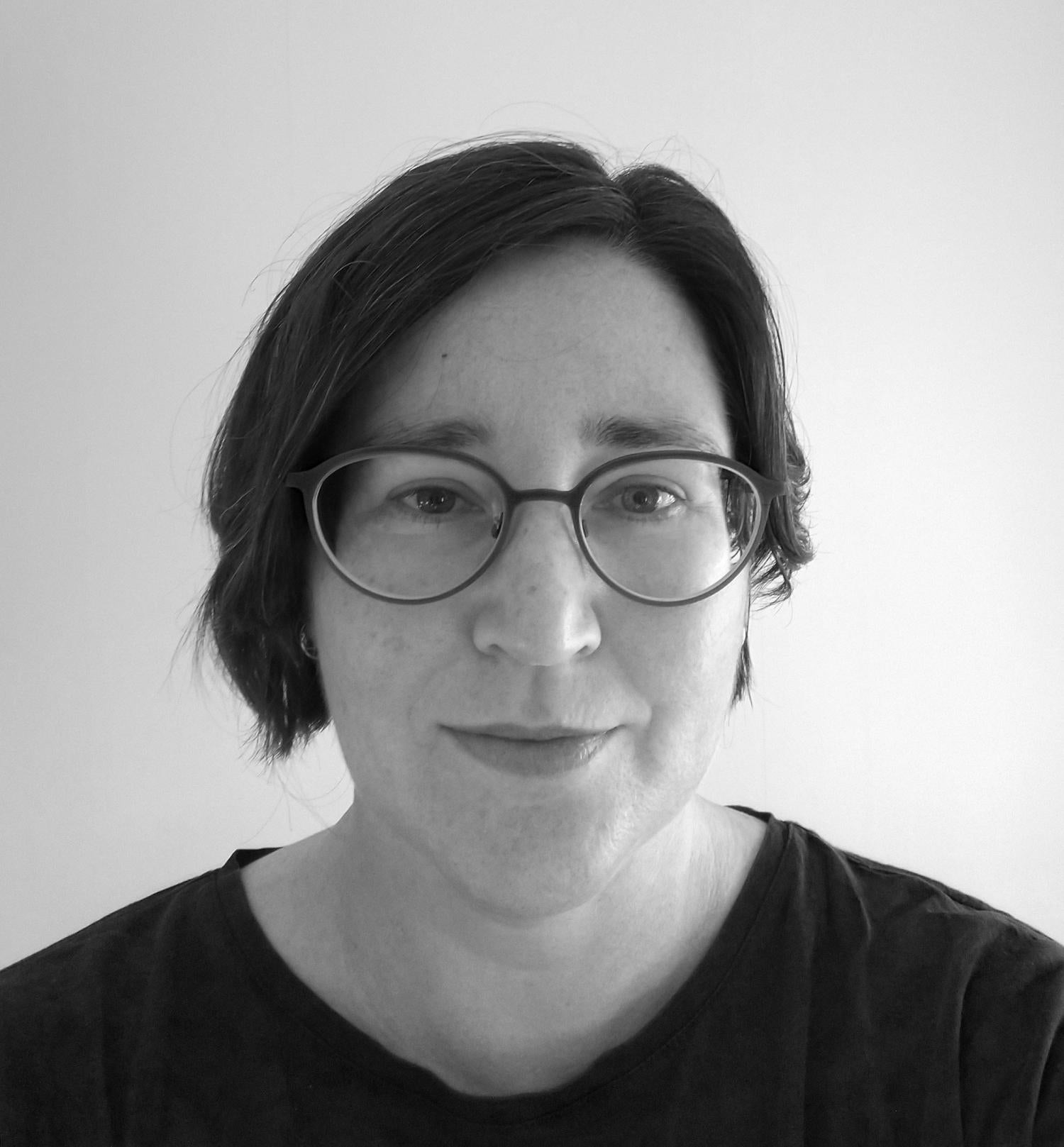 Black and white profile image of a middle-aged woman with a short dark bob. She is wearing glasses and a dark shirt.