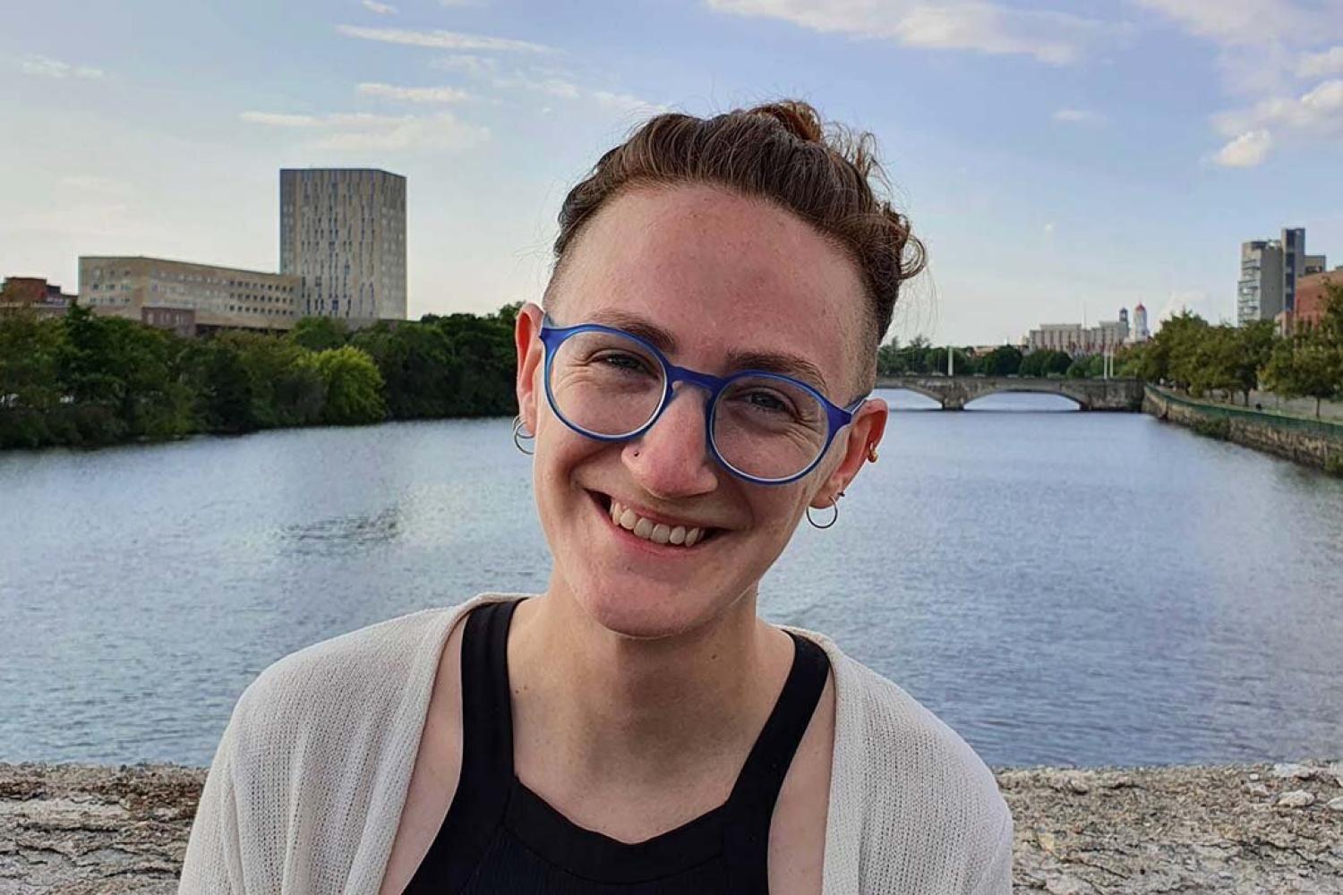 Profile image of a young person smiling. They're wearing blue glasses and a black tanktop.