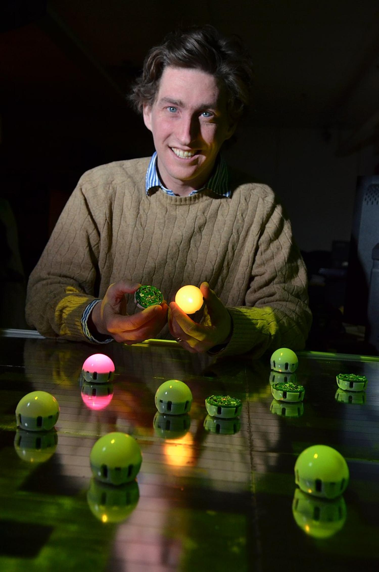 White man with brown hair sitting at a table with a variety of colored light balls in front of him.