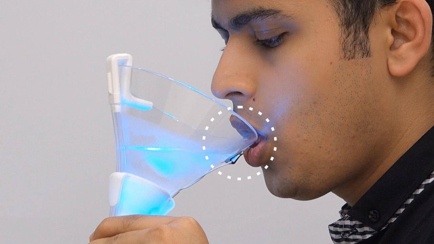 Close up of a light brown man who is drinking from a cup of liquid lit up with cyan light.