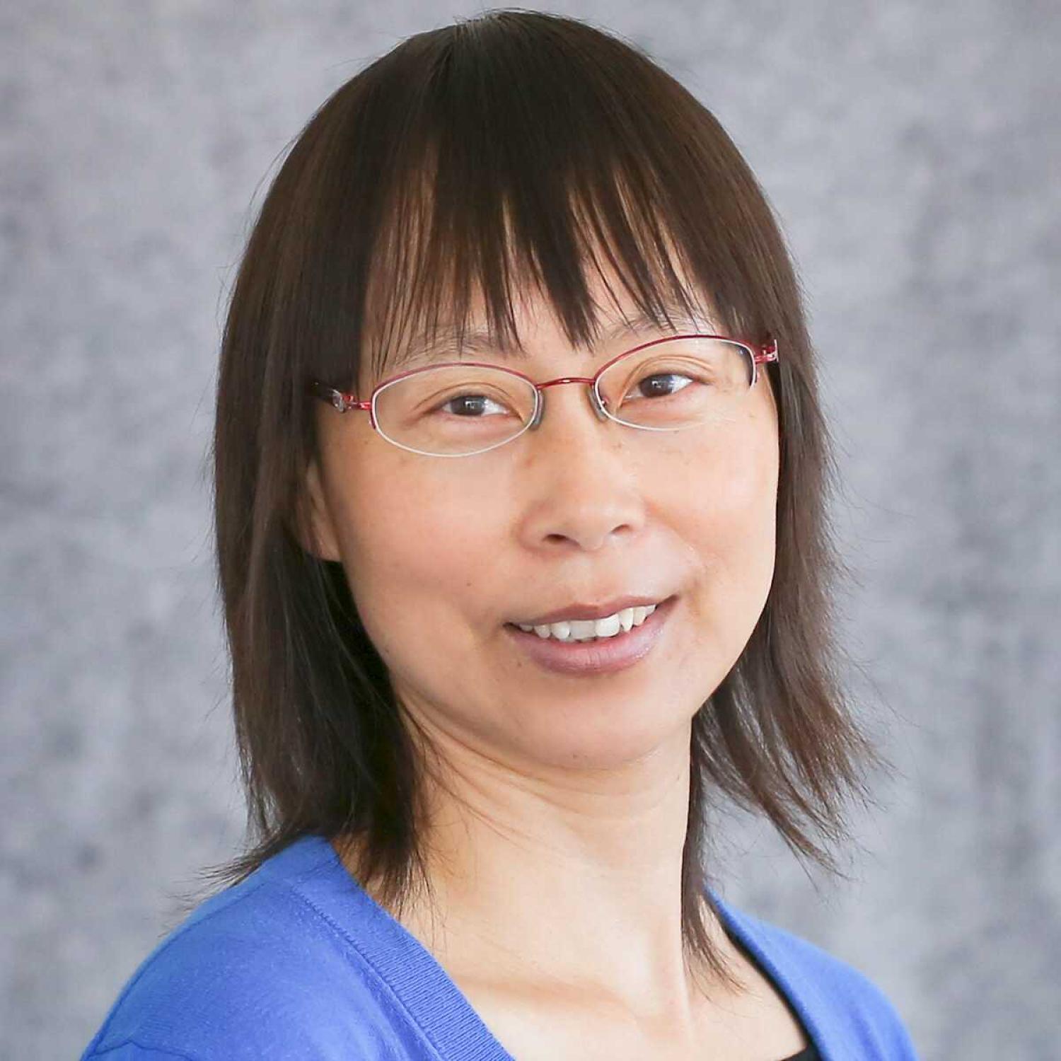 Profile of an asian woman with a brown bob and glasses, smiling.