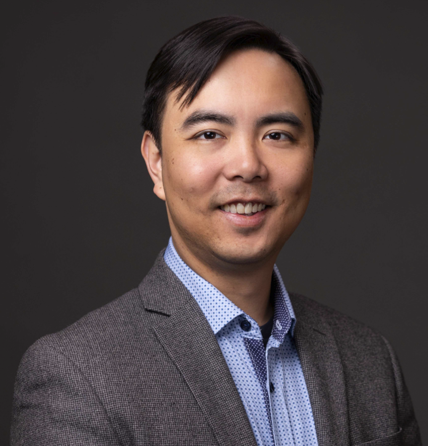 Profile of an asian man with short black hair wearing a gray suit, smiling.