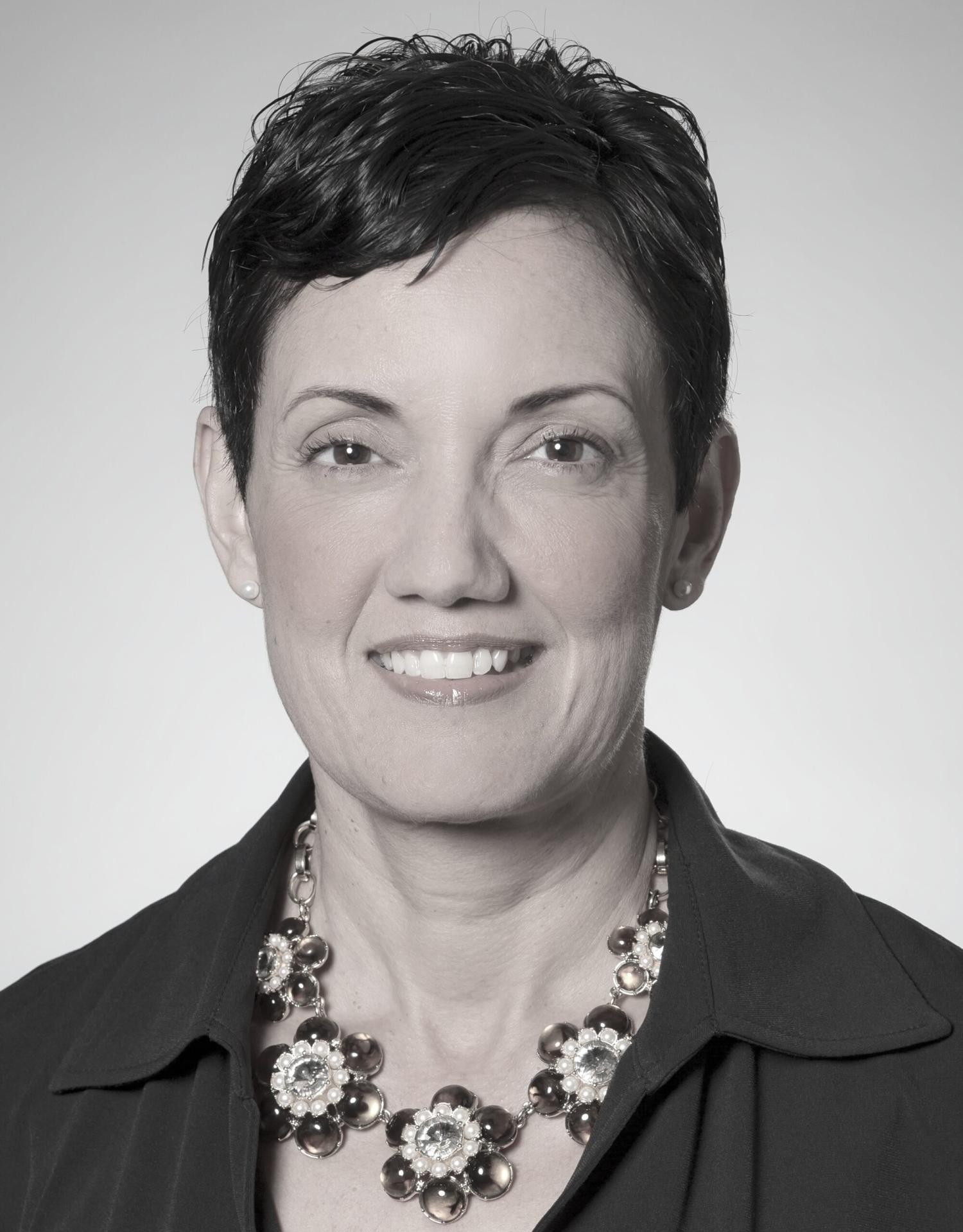 Profile picture of an older woman with short black hair smiling. She is wearing a chunky necklace.