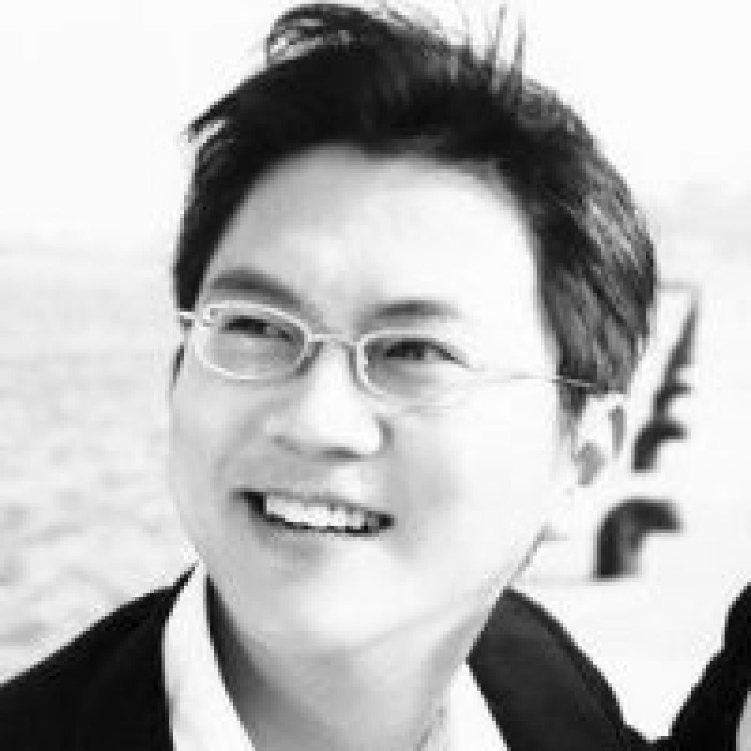 Black and white profile of an asian man smiling. He is wearing glasses.