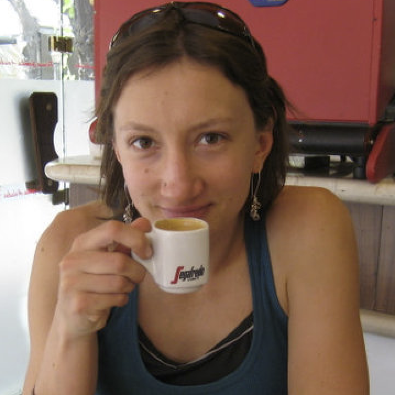 A profile of a young white woman with a brown bob. She is holding a small mug of coffee to her mouth.