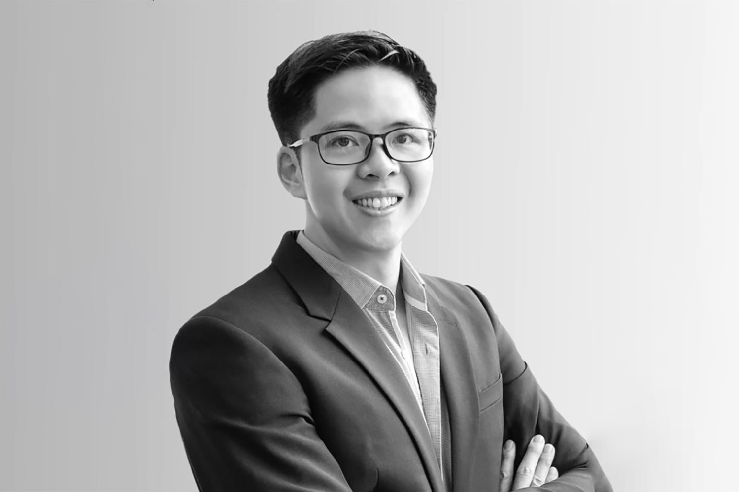 Half-body of a young asian man with short black hair and glasses, smiling.