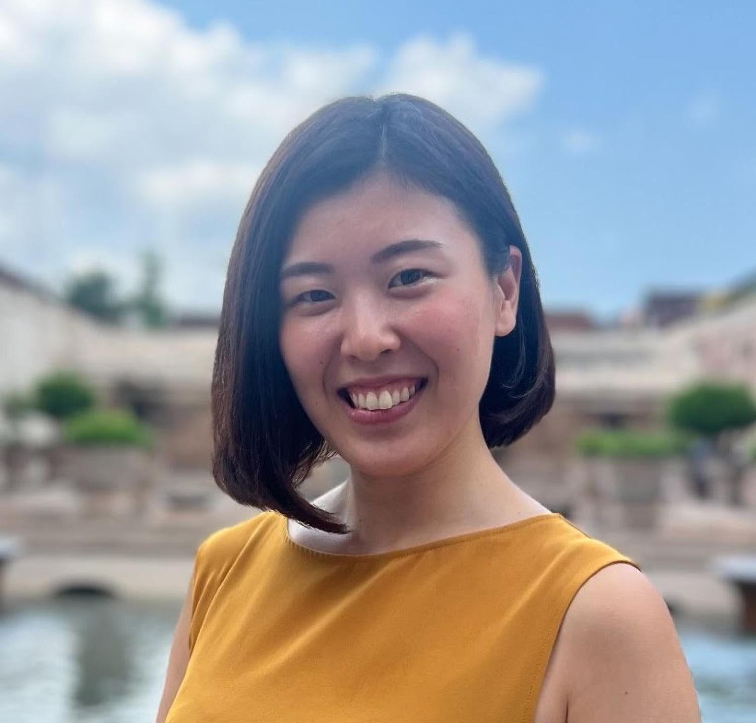 Profile of a Japanese woman with a short black bob smiling at the camera. She is wearing a yellow tanktop.