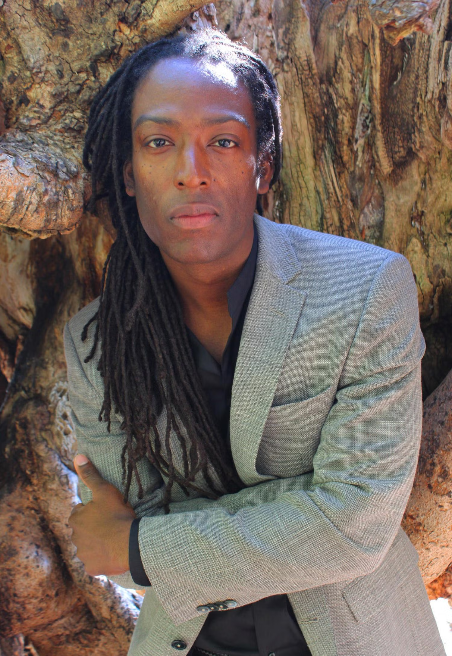 Half-body of a black person with long locs, wearing a gray suit jacket