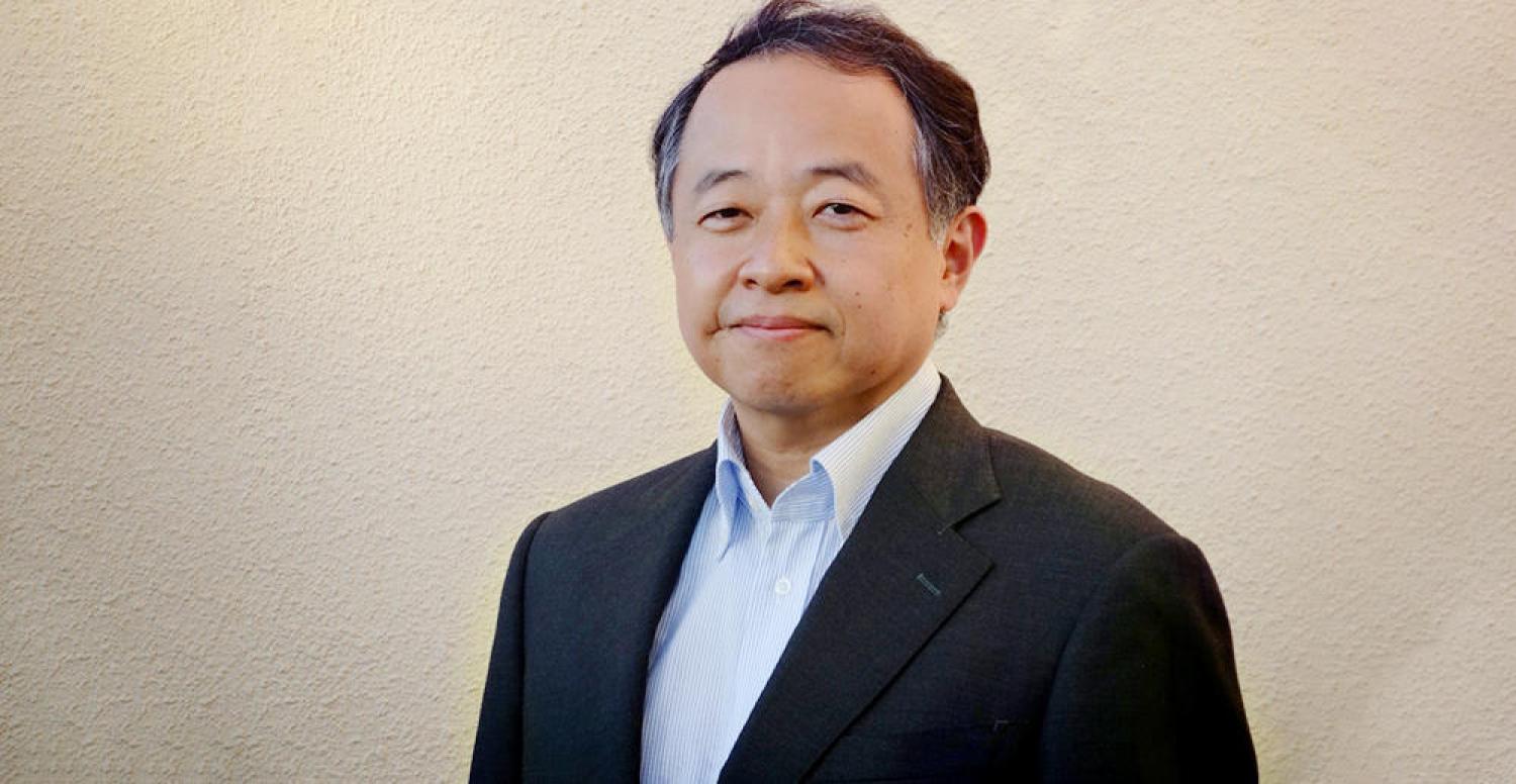 Profile of a middle aged asian man with short black hair, smiling.