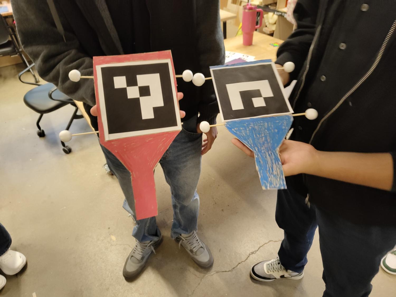 Two people holding up too cardboard controllers that resemble guitar heads