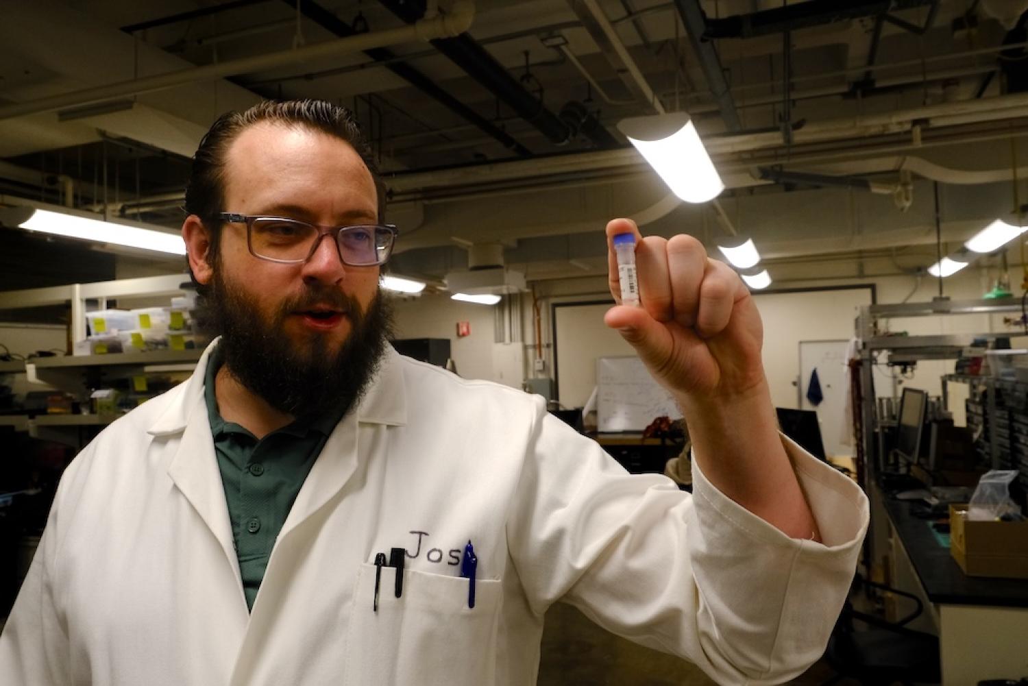 Joshua Johnson in a lab coat holding a small container of DNA