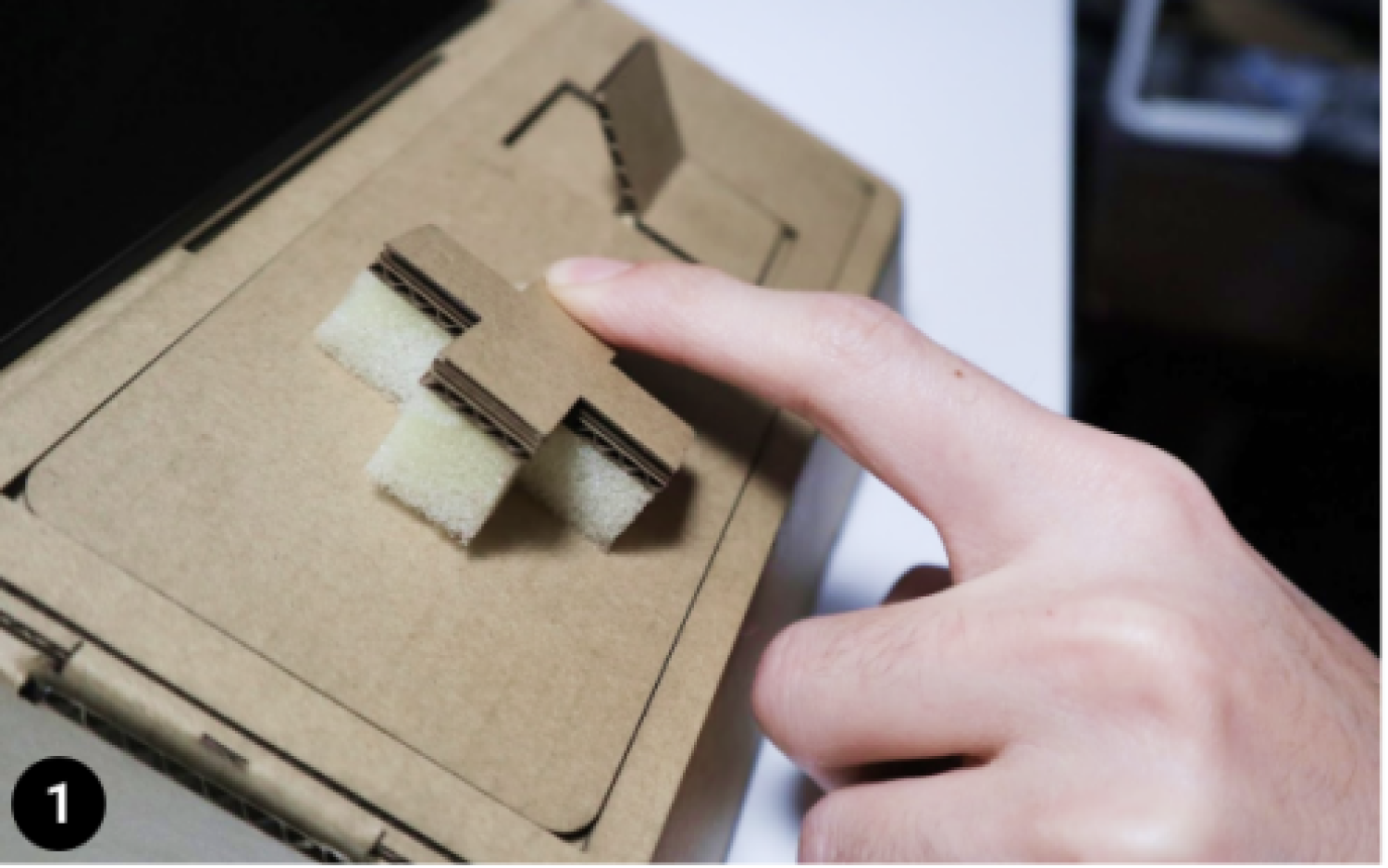 Two hands playing on Tinycade cardboard consoles.