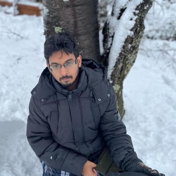 Aseem Visal kneels in the snow by a tree