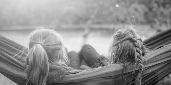 The back of heads of two young girls in a hammock by a lake.