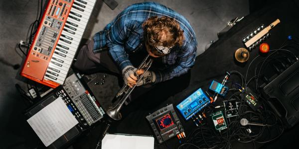 person surrounded by audio equipment playing a horn