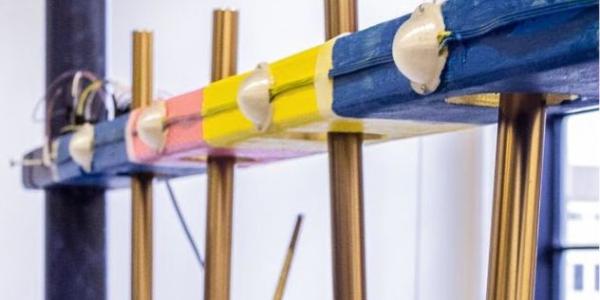 A hand holding a stick used to strike metal pipes with sensors attached to them.