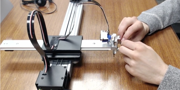 A user gripping the mechanical arm of a pen plotter to experience kinetic content.