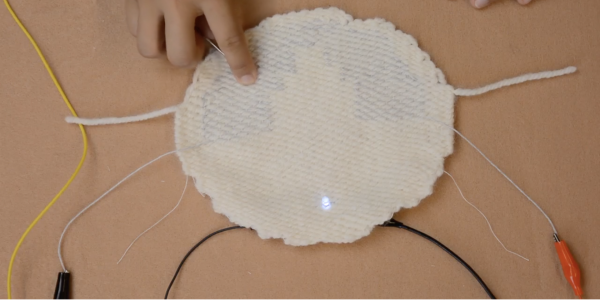 A smart fabric being touched, causing an LED light to turn on.