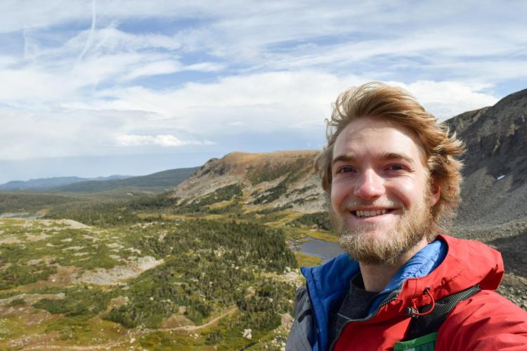 Nate Bennett in a jacket in front of a wide expanse of mountains and sky.