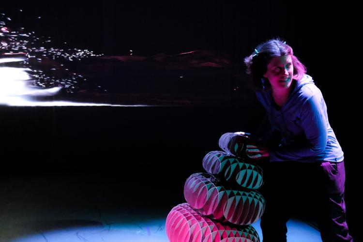 A student adjusts the cairn under dramatic lighting as animations are projected behind