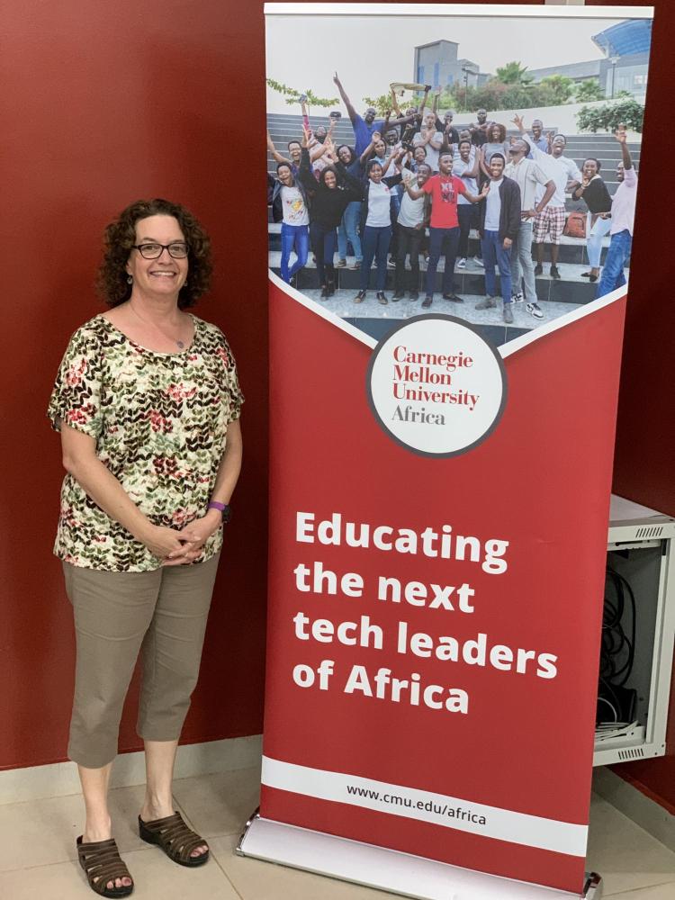 Aileen Pierce standing next to a sign that reads "educating the next tech leaders of Africa."