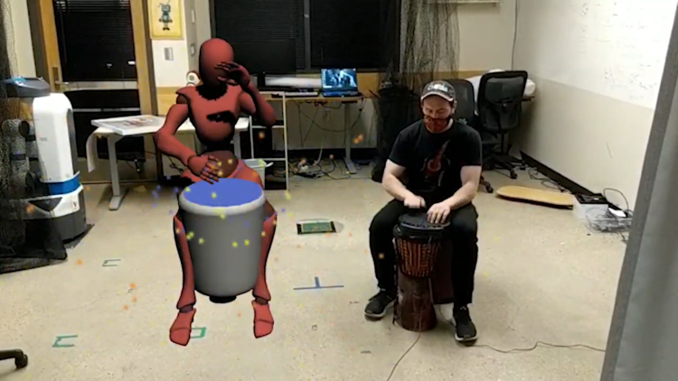 Torin Hopkins beats on a drum next to an avatar also beating on a drum