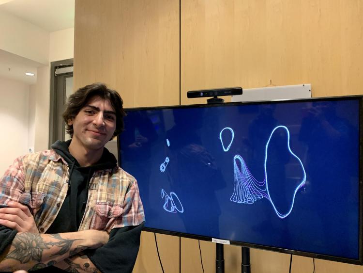 Arnon Naeini stands in front of a computer screen which shows his ::body project.