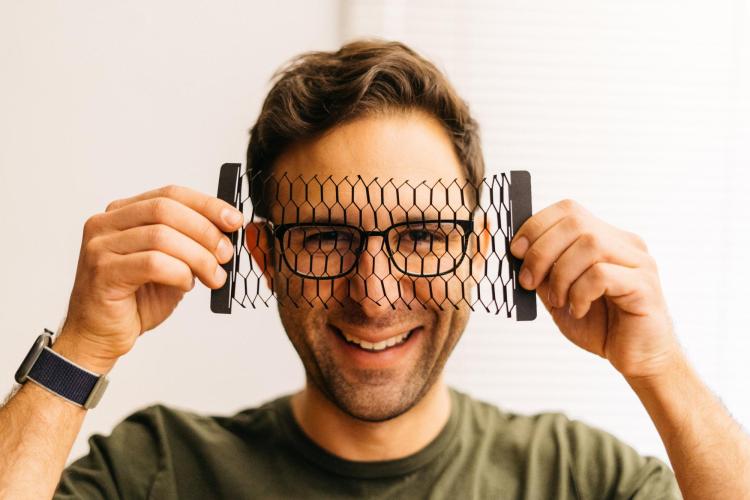 Bryan holds diamond-patterned laser-cut carbon-coated paper in front of his face.