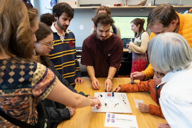 Community members stand around a table playing with Collaborator together at EXPO 2024 in the Audio Frequency Lab