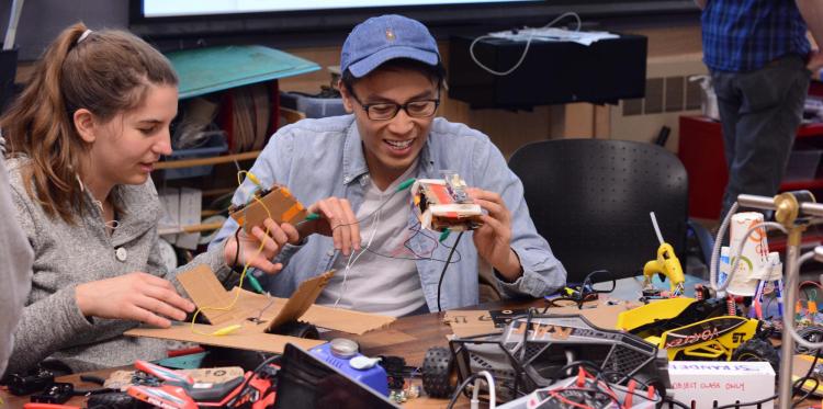 Two students smile as they hold up the circuits they built from cardboard and micro:bits