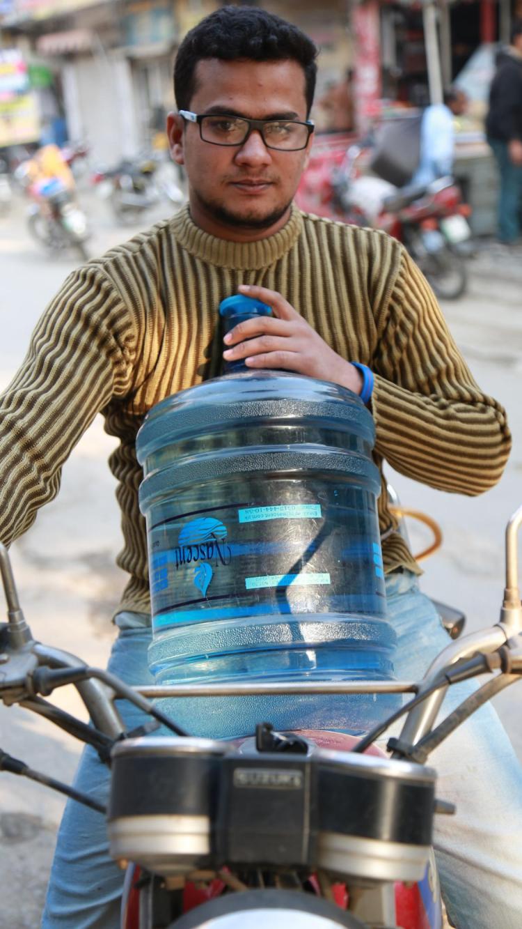 Man on motorcycle holding large jug of water from Water ATM