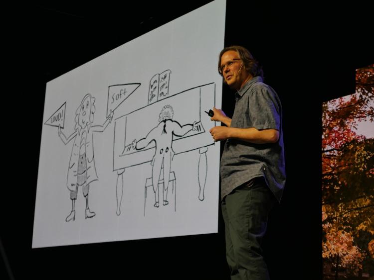 Michael Theodore points to a large cartoon drawing that he drew of a man at a piano and another man holding loud and soft signs.