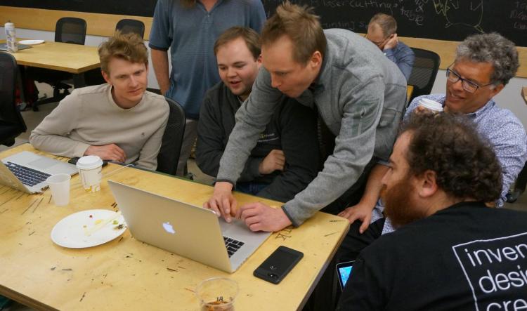 Tom Ball demonstrates MakeCode on his computer, surrounded by workshop participants.