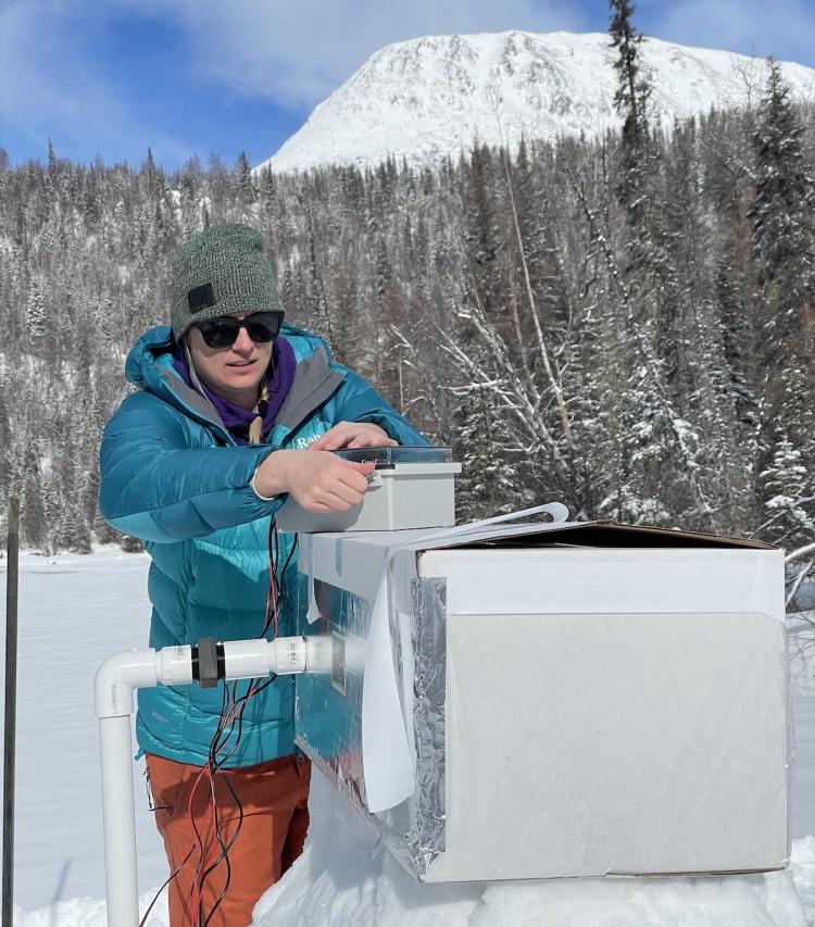 Cold box prototype in a snowy field with trees and mountain in the background