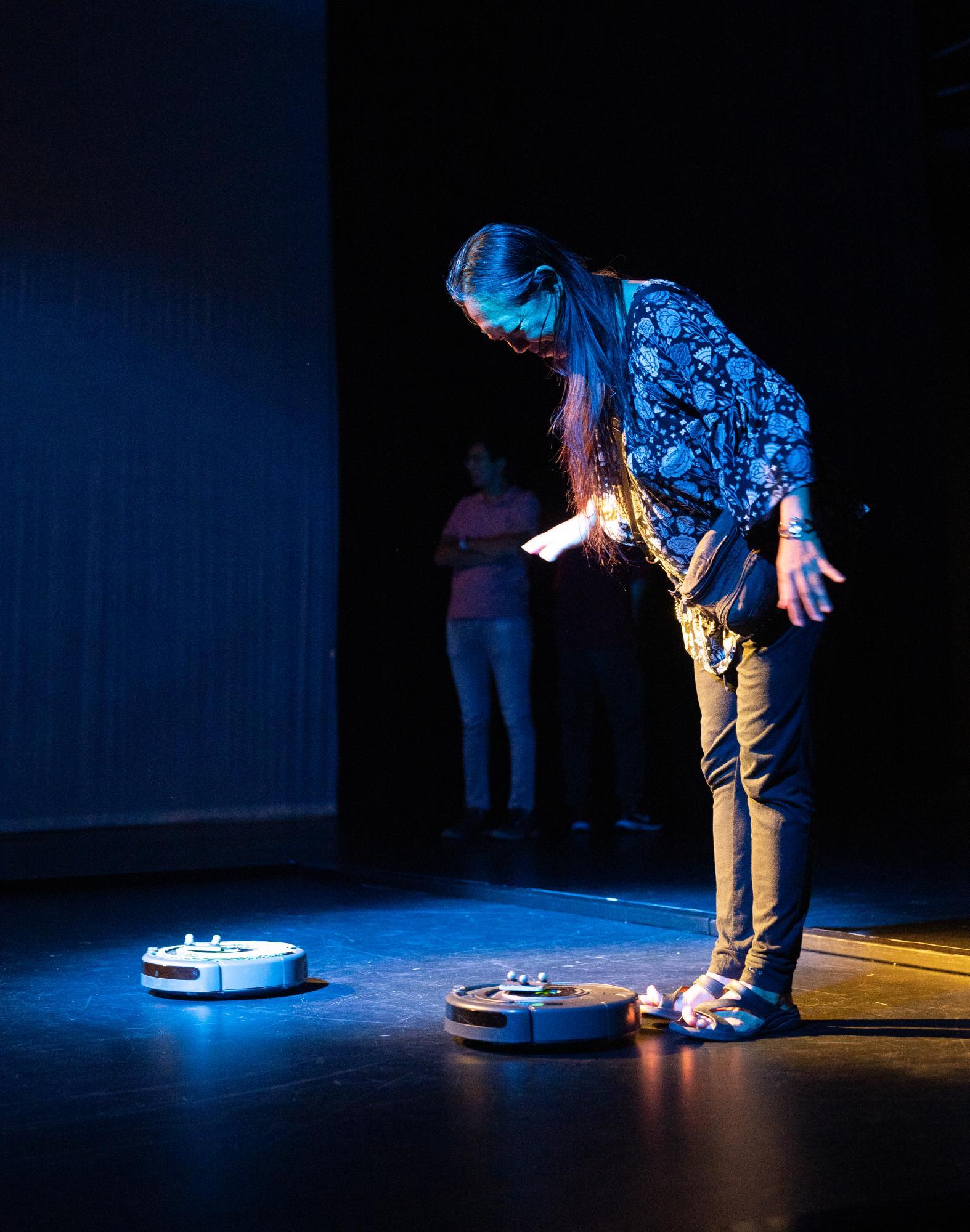 woman standing over a robot looking down at it in blue light