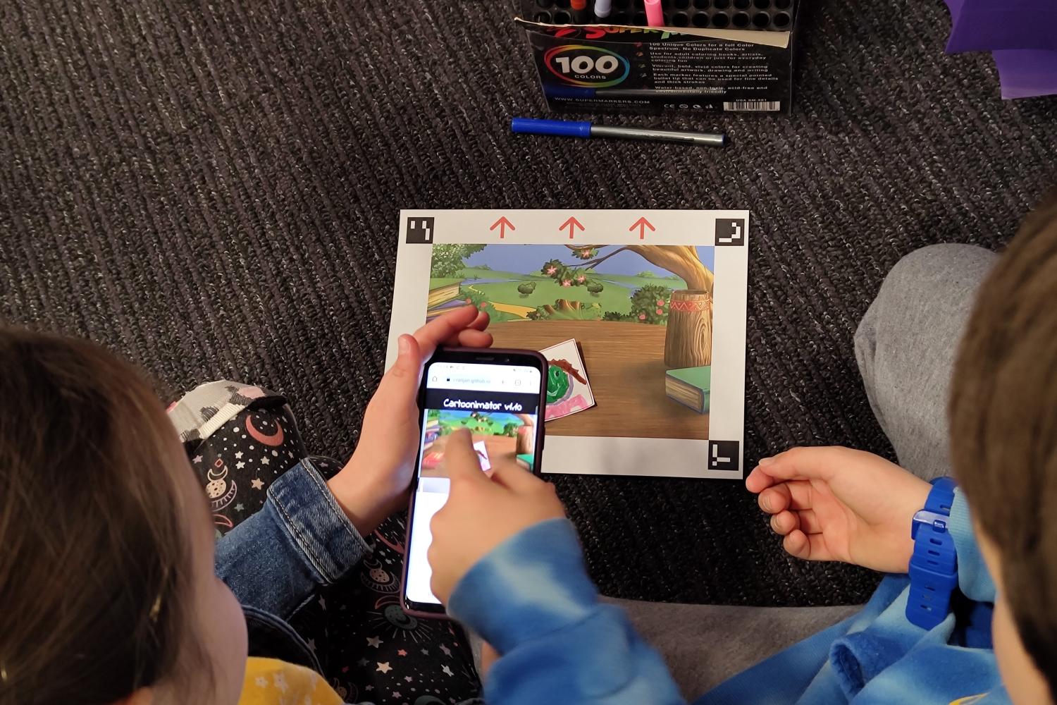 Two people holding phone up to cartoon on paper