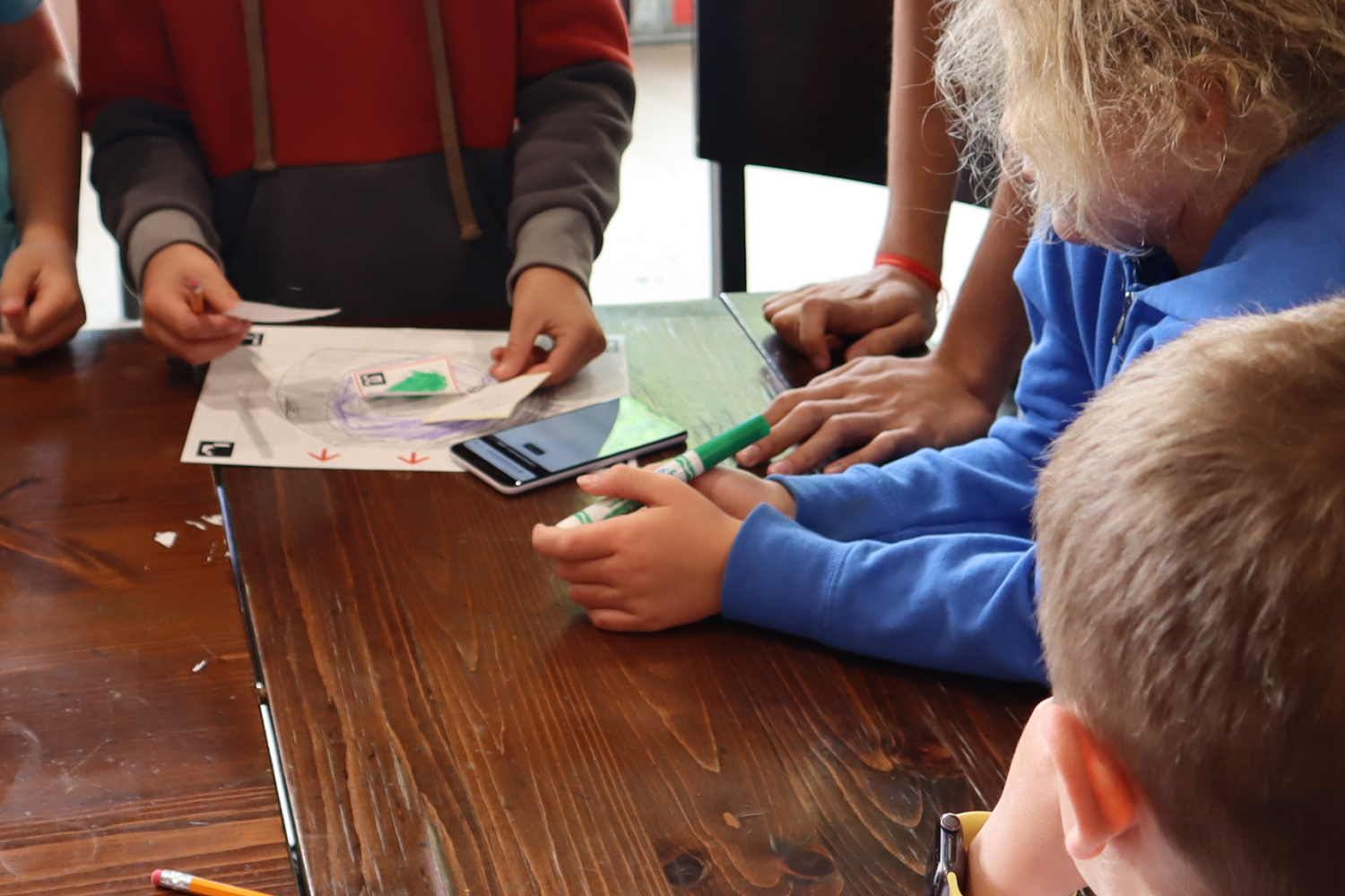 Children at a table watching person lay out a paper scene